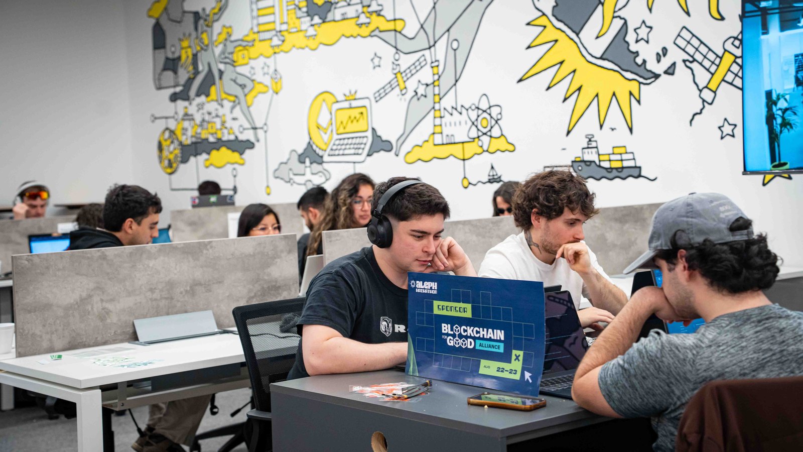 Horas de hacking en el Aleph Hub, con la placa de Blockchain for Good Alliance en la mesa